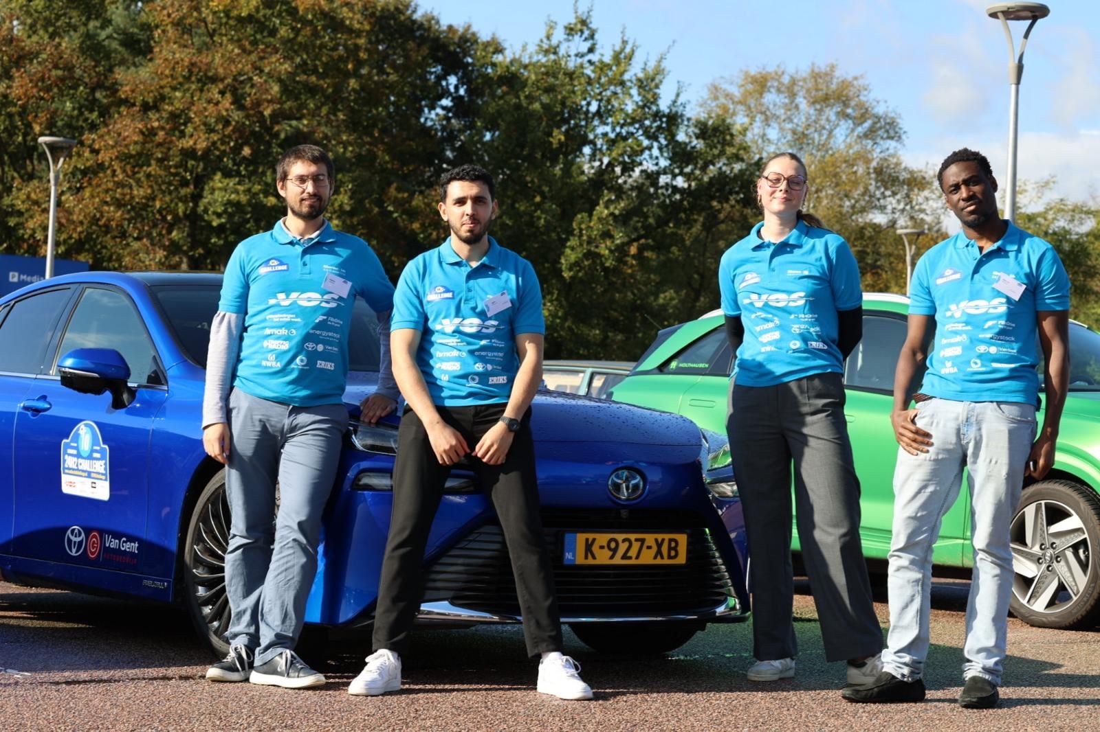 Four members of the 24H2 Challenge team in blue polo shirts in front of two hydrogen cars